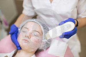 Close up of cosmetologist hands in blue sterile gloves holding ultrasonic skin equipment for cleaning female client face