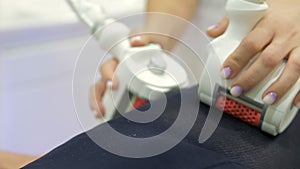 A close-up of a cosmetologist-therapist gives a man in a special black suit an anti-cellulite LPG massage in a beauty