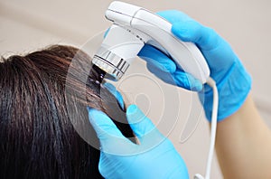 A close-up of a cosmetologist-trichologist diagnoses the condition of the patient& x27;s hair using a trichoscope.