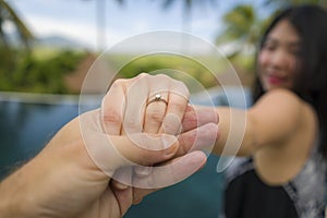 Close up couple hands holding in love with Asian woman showing diamond engagement ring celebrating marriage proposal at beautiful