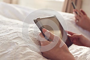 Close Up Of Couple At Home In Bed Using Digital Tablet And Mobile Phone During Covid 19 Lockdown