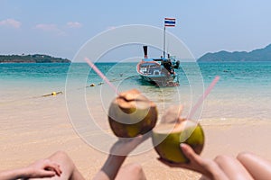 Close-up Of Couple`s Hand Holding Coconut With Drinking Straw In Front Of Idyllic