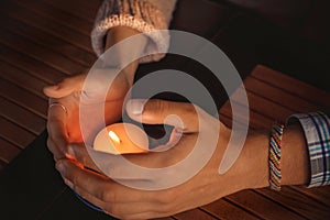 Close up of couple`s hands cupped around a burning candle. Hands of young man and woman that protect the flame of a candle. Love