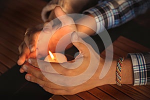 Close up of couple`s hands cupped around a burning candle. Hands of young man and woman that protect the flame of a candle. Love