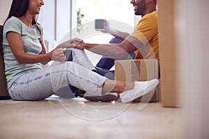 Close Up Of Couple Taking A Break Sitting On Floor Of New Home With Hot Drinks On Moving Day