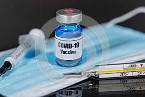 Close up of COVID 19 vaccine vial, syringe, face mask and thermometer. Isolated. Corona virus