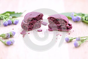 Close up crack purple macaroon with purple flower and green leaves on wood table background