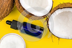 Close up of cracked Coconuts and glass eyedropper bottle and coconut oil isolated on yellow background