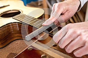 Close up of a craftsman`s hands, filing the frets of a guitar