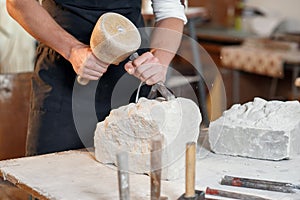 Bearded craftsman works in white stone carving with a chisel. Creative workshop with works of art.