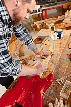 Close-up of a craftsman sanding a guitar neck in wood at workshop