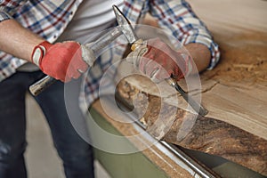 Close up of craftsman working with chisel while cutting wooden plank in carpentry workshop