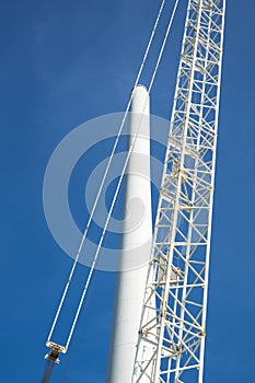 Close up, crane and pole of windmill, against blue sky.