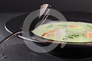 Close-up cream broccoli soup with shrimp in a beautiful black plate on a dark background. Seafood dish. Selective focus.