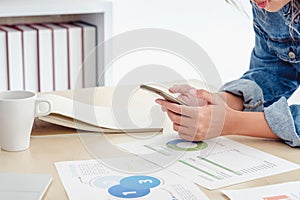 Close up creative director use mobile phone at desktop table at office when planning work with datasheet