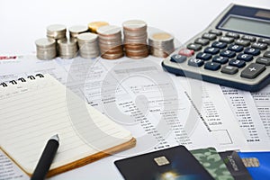 Close up of a credit cards with credit card statements, pen, notebook, stack of coins and calculator on white background