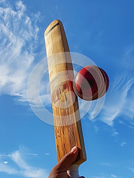 Close-up of cricket wooden bat hitting red leather ball against blue background Sunny day competition