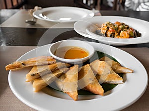 Close up of crispy spring roll stuffed with prawns and pork on a white plate in a restaurant.