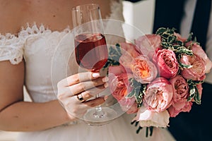A close-up of a cropped frame of a bride in a white dress is holding in her hand a wedding bouquet of pink peonies, and