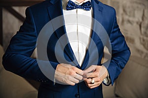 Close-up of a cropped frame of a man buttoning his stylish jacket over a button, wearing a white shirt and a bow tie, a