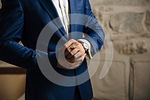A close-up of a cropped frame of a man in an expensive classic costume looks at his watch. The businessman is in a hurry