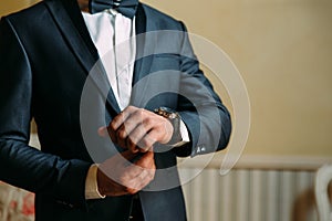 A close-up of a cropped frame of a man in an expensive classic costume looks at his watch. The businessman is in a hurry