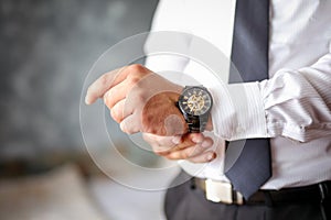 A close-up of a cropped frame of a man in an expensive classic costume looks at his watch.