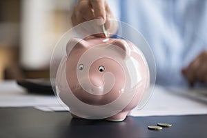 Close up cropped image female hand putting coin in piggybank