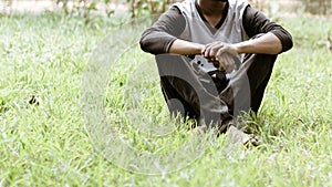 Close up Cropped image of young man in casual clothing sitting over green grass in the park at morning time of day. Front view.