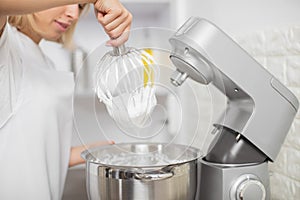 Close up cropped indoor shot of professional female chef, making desserts at her pastry shop, remowing mixer whisk with photo