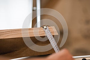 Close-up cropped male carpenter hand using ruler tape to measure wood timber or board, fixing, preparing to cut working