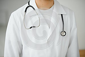 Close-up, cropped man in a white medical coat. The doctor writes something in the patient`s card. Light photo
