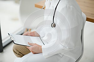 Close-up, cropped man in a white medical coat. The doctor writes something in the patient`s card. Light photo