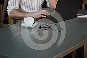 Close up cropped photo. Adult man sits in cafe at daytime and using the laptop for the remote work