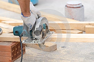 Close up cropped photo of adult unrecognizable professional using electric saw build new home. Man in white protective gloves cut