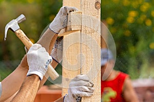 Close up cropped photo of two man holding plank board by hand installing special house hold construction using hammer and nails