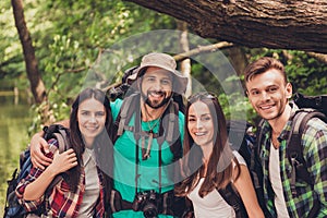 Close up cropped portrait of four cheerful friends in the summer nice wood. They are hikers, walking and picking place for campin photo