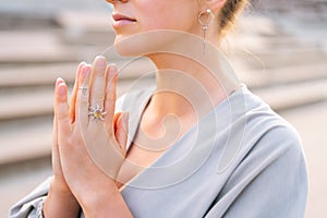 Close-up cropped shot of calm young woman practicing yoga performing namaste pose with closed eyes outside in city park.