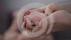 Close-up cropped shot of loving mother massaging newborn infant baby feet with thumbs tender touch parenting. Closeup of
