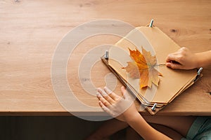 Close-up cropped shot of thinking little child girl holding beautiful dry maple leaf to create herbarium diy at home.