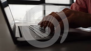 Close-up cropped shot of unrecognizable business man typing on laptop computer sitting at office desk on background of