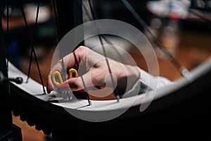 Close-up cropped shot of unrecognizable female cycling repairman hands checking bicycle wheel spoke with spoke key