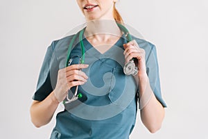 Close-up cropped shot of unrecognizable female doctor in green medical uniform with stethoscope around neck.
