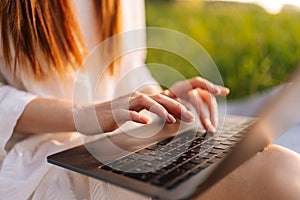 Close-up cropped shot of unrecognizable female freelancer working typing on laptop computer sitting on beautiful field