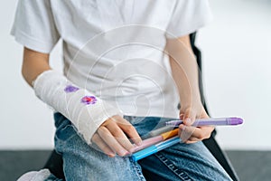 Close-up cropped shot of unrecognizable little girl drawing cute image with colorful marker on broken arm wrapped in