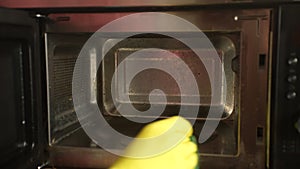 Close-up cropped shot of unrecognizable man wearing yellow household gloves wipe inside of microwave with cleaning