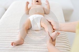 Close-up cropped shot of unrecognizable mother or masseuse massaging foot of infant baby. Little infant receiving feet