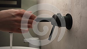 Close-up cropped shot of unrecognizable woman opening faucet and washing hands over white sink with clean running water