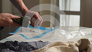 Close-up cropped shot of unrecognizable young male dad putting folded children clothes in vacuum compression bag for