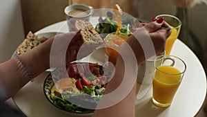 Close-up cropped shot of unrecognizable young woman spreading apricot jam on slice of bread with fork at table with